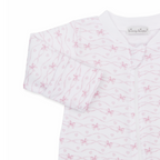 A white long-sleeve baby girl zip-up footed sleeper closeup with a delicate light pink bow and heart pattern and Kissy Kissy brand label.