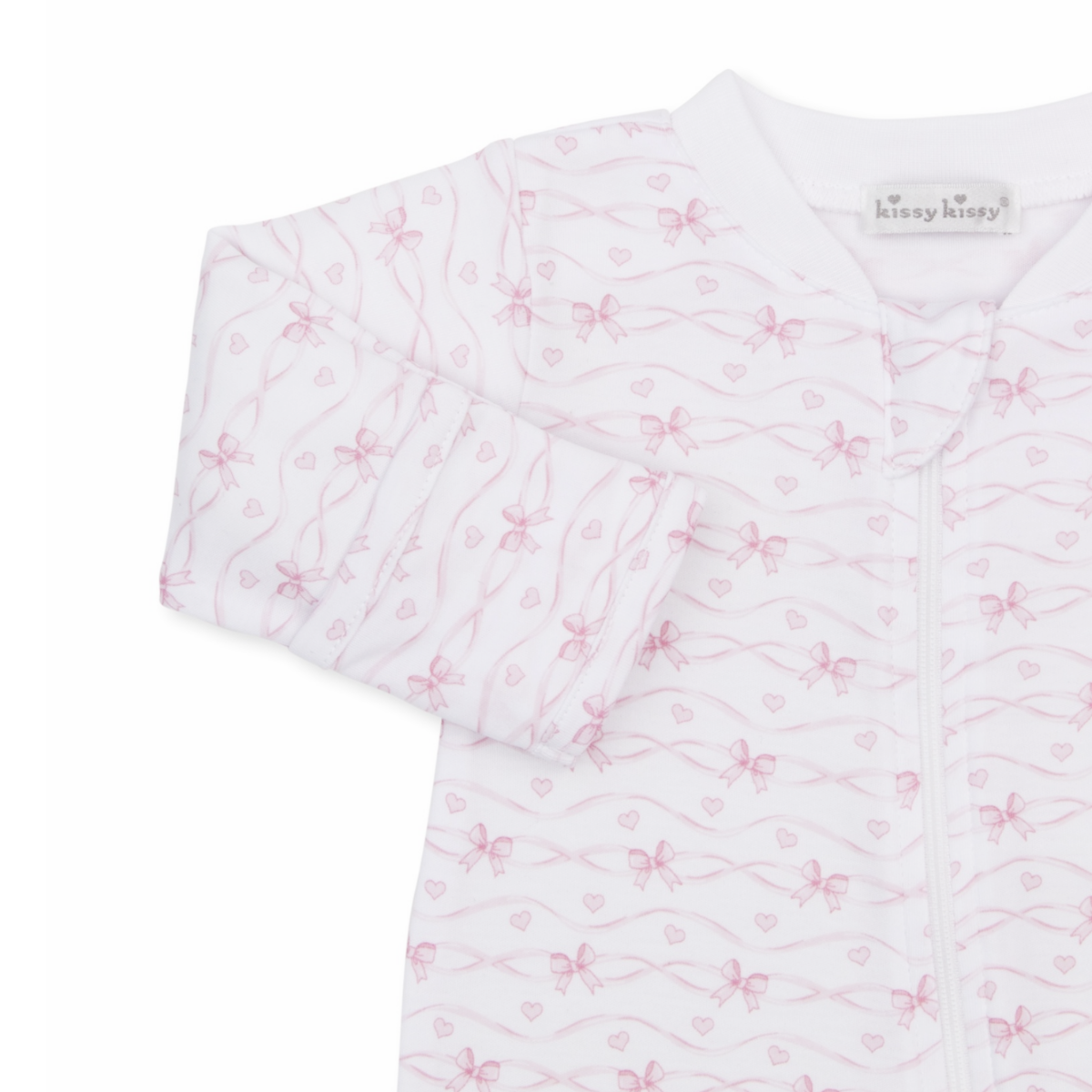 A white long-sleeve baby girl zip-up footed sleeper closeup with a delicate light pink bow and heart pattern and Kissy Kissy brand label.