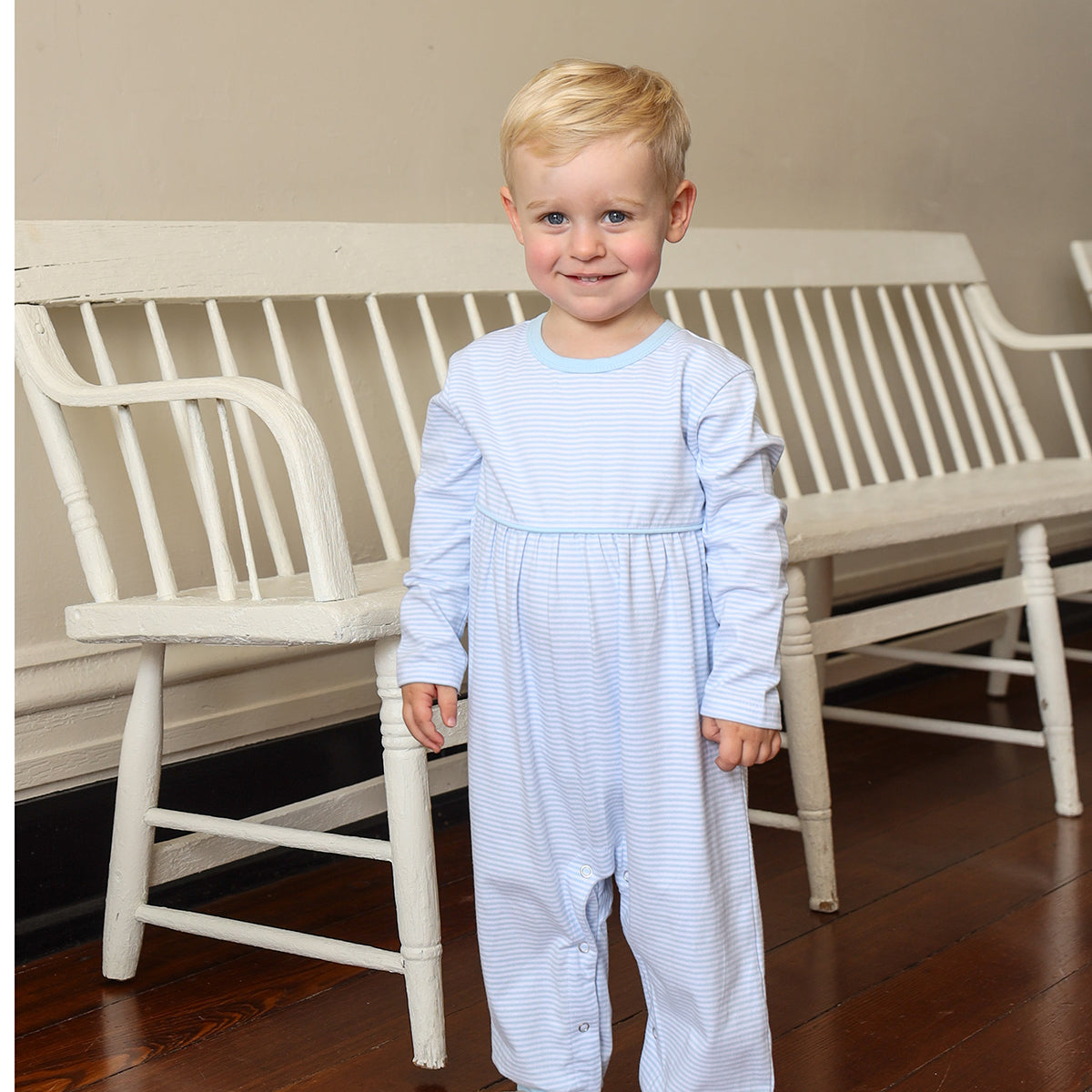 Child wearing a light blue striped outfit standing in a room with white furniture.