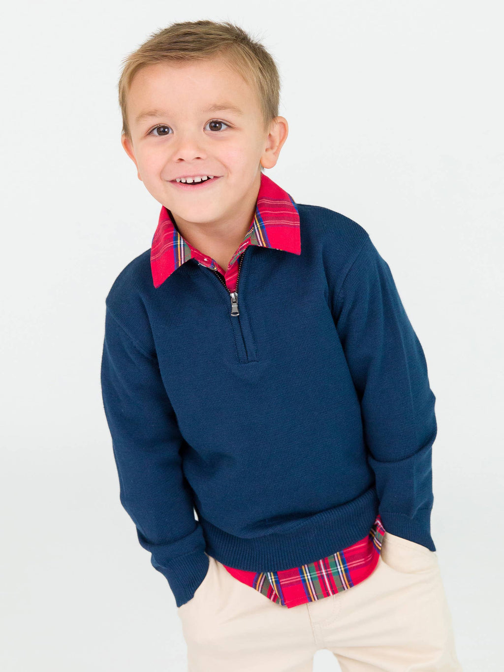 Young boy wearing a navy sweater over a plaid shirt with a white background