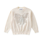 An off-white long-sleeve knit sweater featuring a large, textured bow embellished with shimmering silver rhinestones on the chest, displayed against a solid white background.