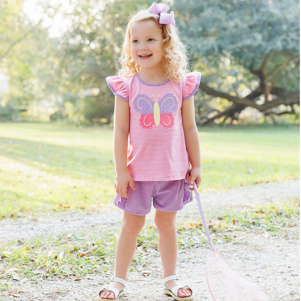 Toddler girl wearing a pink stripe and lavender shorts outfit with a butterfly applique and flutter sleeves.