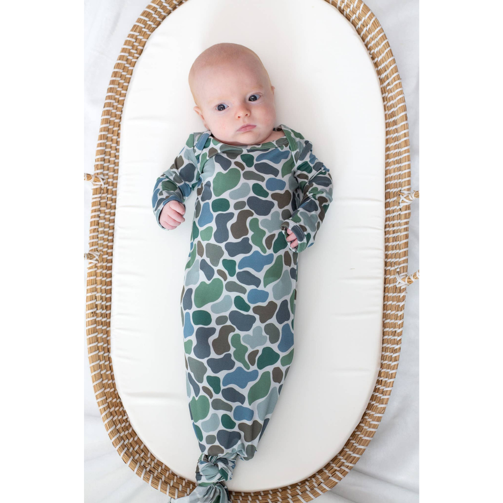 Baby wrapped in a blue and green patterned swaddle blanket lying on a white surface.