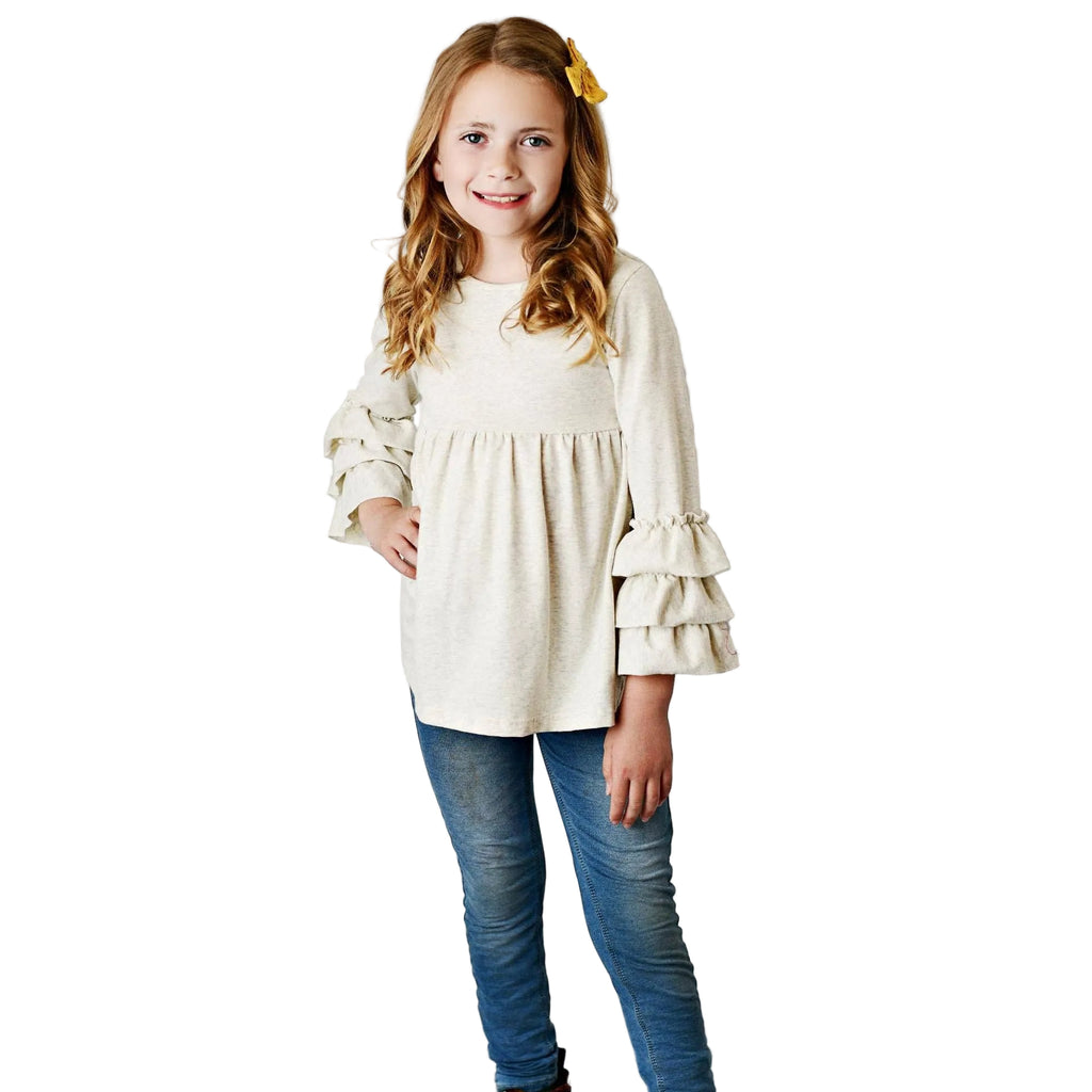Young girl wearing a white blouse with ruffled sleeves, blue jeans, and brown boots against a gray background.