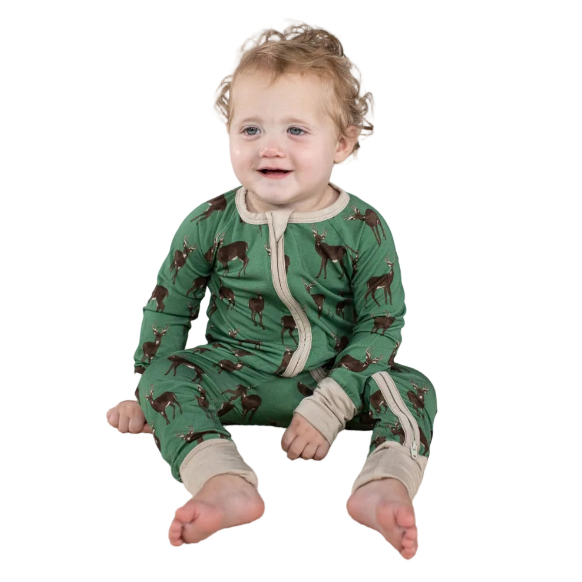 Baby wearing a green onesie with animal patterns sitting on a beige blanket.