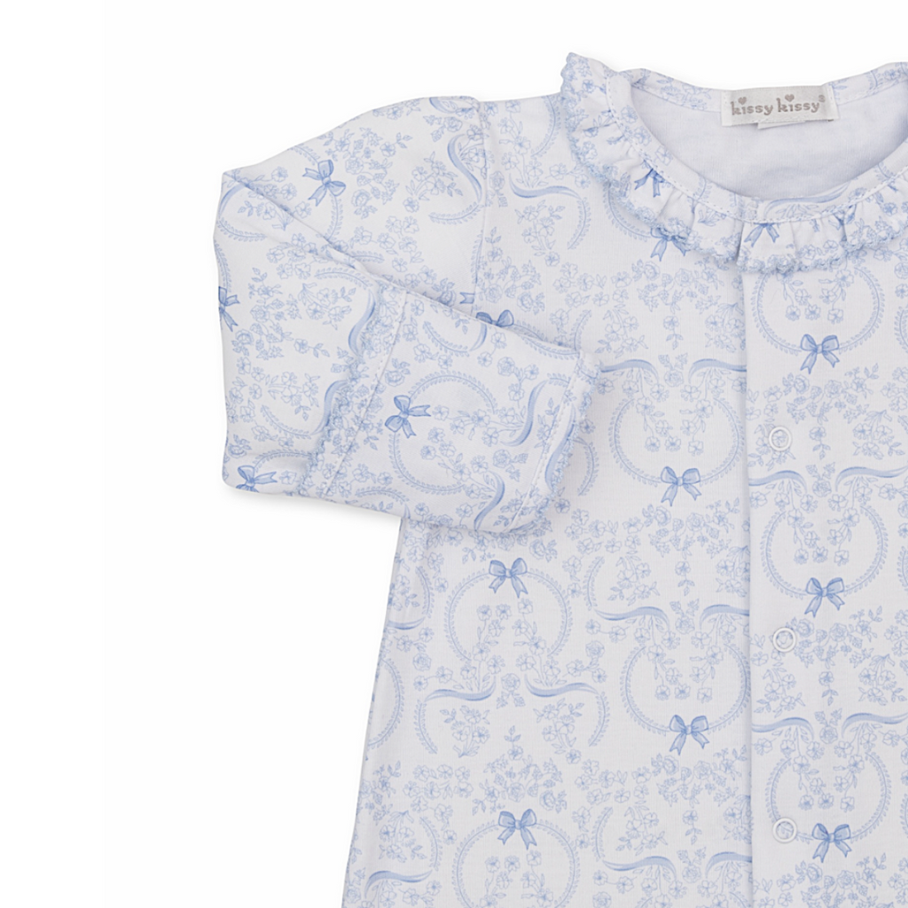 Closeup of a baby girl gown with ruffled collar and blue bows and floral pattern.