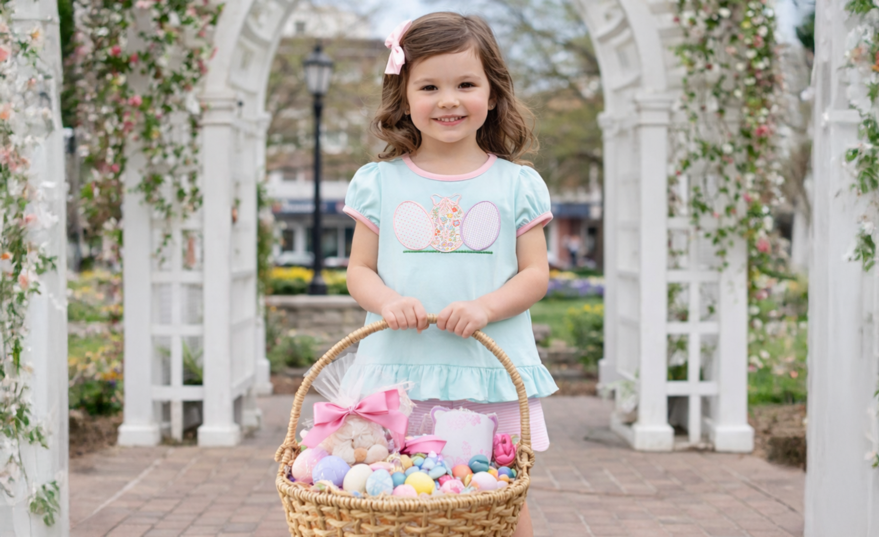 Young girl wearing an appliqued Easter outfit holding a basket of Easter eggs in a garden setting
