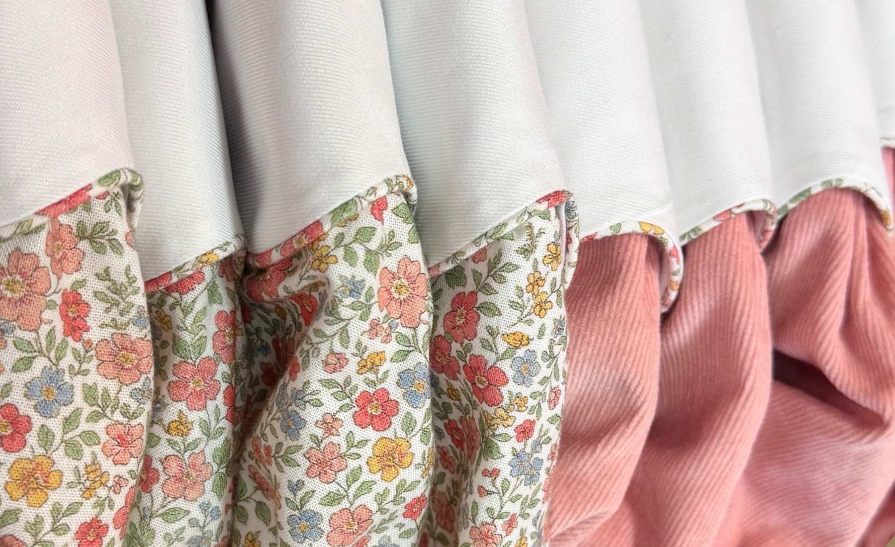 Close-up of a little girl boutique fall dresses featuring a multicolor floral print alongside a pink corduroy fabric.