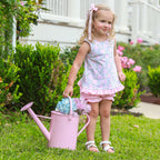 Little girl wearing a floral knit bloomer set carrying a pink watering can with hydrangeas.