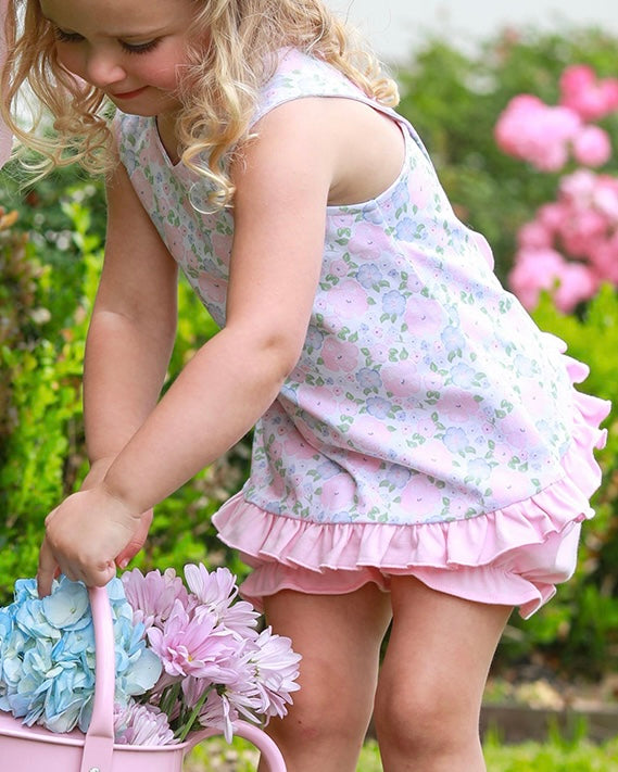 Child in a spring floral bloomer set holding flowers in a garden