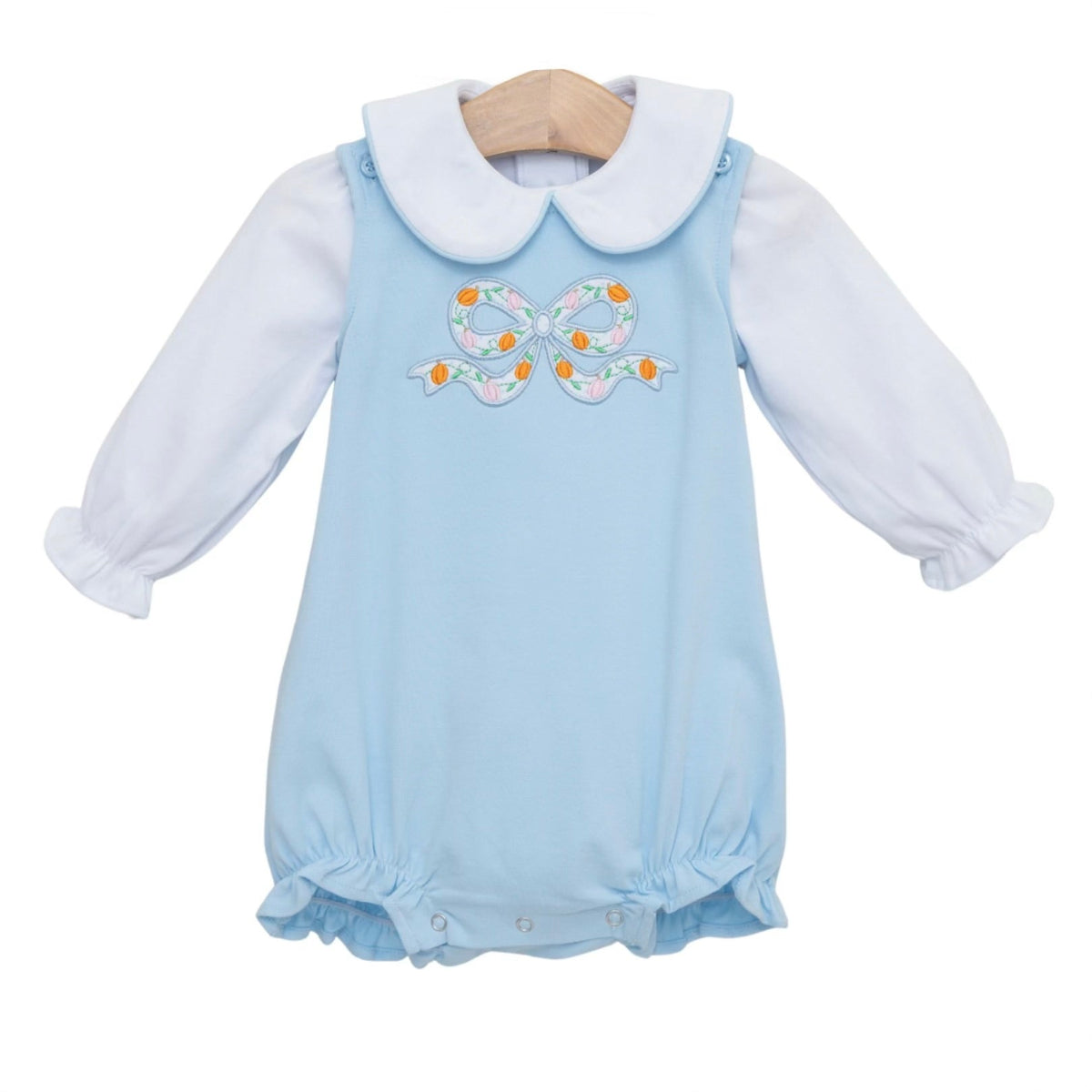 A baby girl's light blue long-sleeve bubble paired with a white long sleeve knit shirt and appliqued embroidered bow with pumpkins.