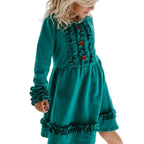 Child wearing a teal dress with ruffles in a bright room.
