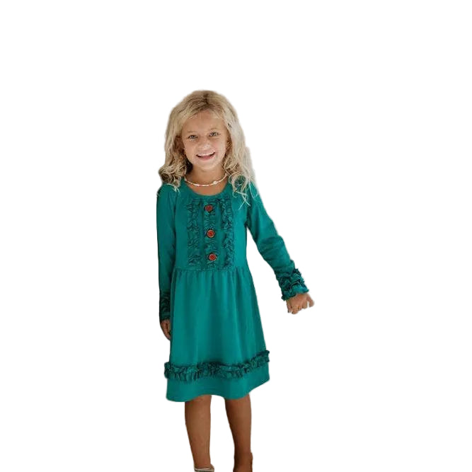 Young girl in a teal dress standing in a room with a window.