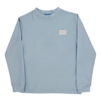 A light blue long-sleeve crewneck t-shirt with a small white patch on the left chest.