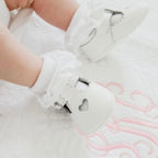 White baby girl shoes with a heart cutout and T-strap design.
