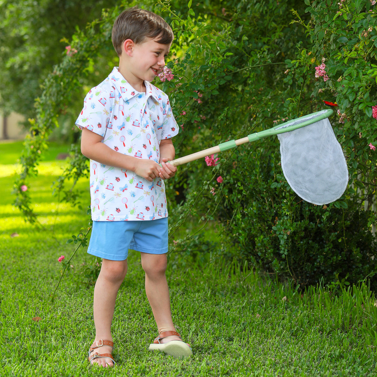 Boy catching bugs in a net while wearing an insect print polo shirt and blue shorts knit outfit.