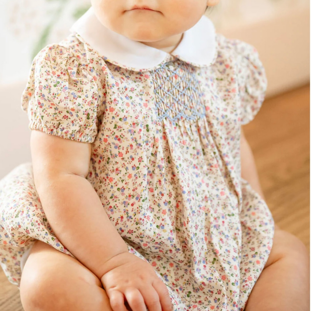 Baby girl wearing a cotton bubble in a fall floral print, white Peter Pan collar, puff sleeves, smocked chest panel, elastic leg openings, and snap closure.