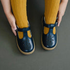 Girl wearing navy blue T-strap everyday shoes with perforated design