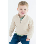 Child wearing a beige sweater over a green shirt with blue jeans on a white background