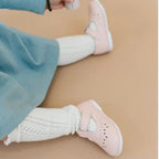 Little girl’s feet wearing light pink T-strap Mary Jane shoes with a perforated design and white knee socks