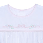 Close up of a white baby sleep sack with a round neckline and delicate light pink bow and floral shadow embroidery across the chest.