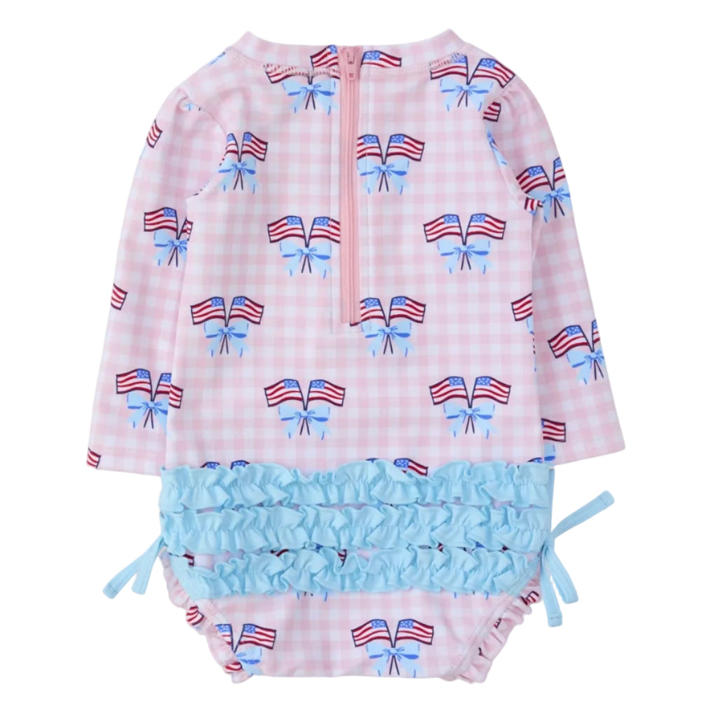Back view of a baby girl long sleeve one piece swimsuit with patriotic American flag and bow pattern, zipper back, and ruffled bottom.