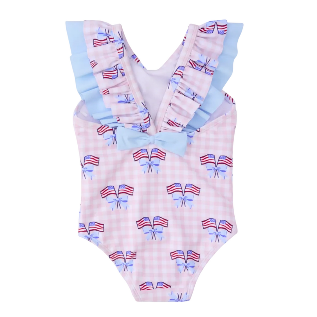 Back view of a girl’s one piece patriotic bathing suit with bow and American flag pattern on a pink gingham check background with blue bow.