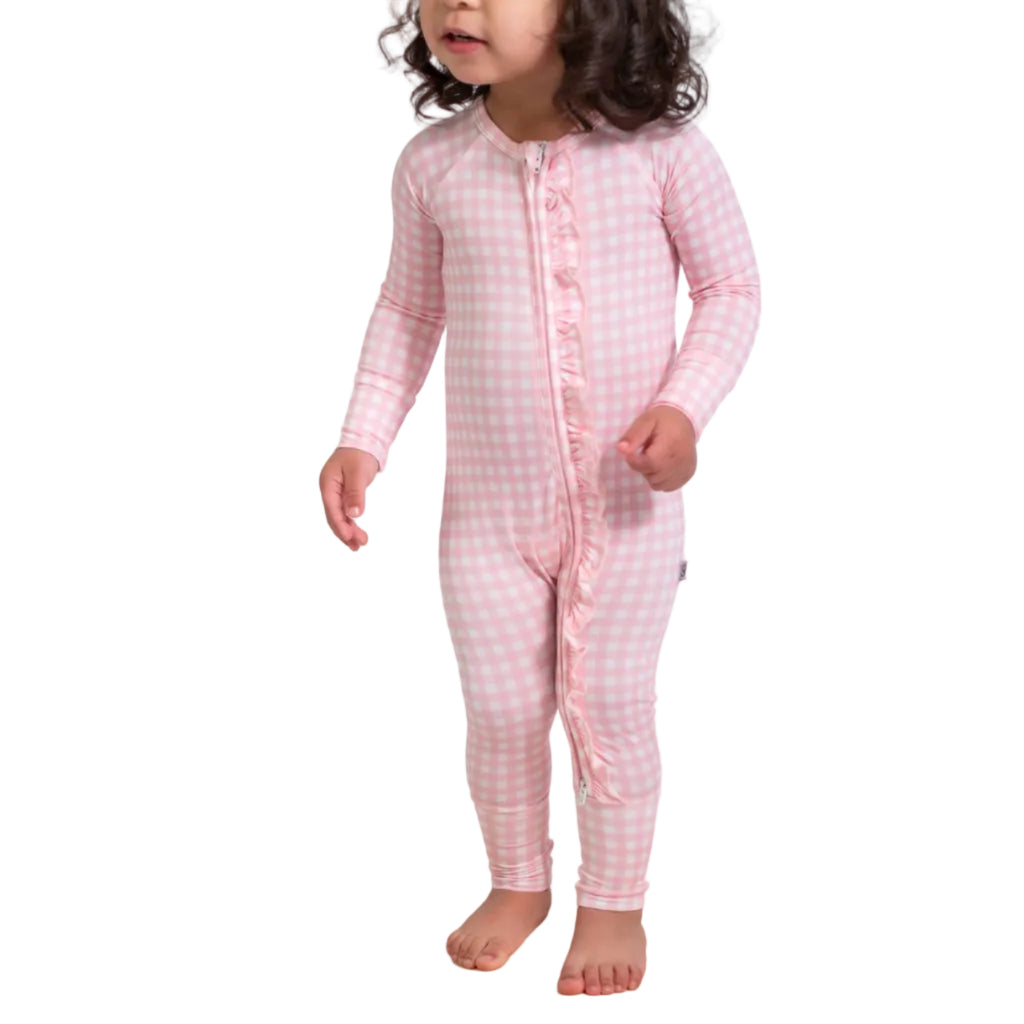 Child wearing a pink checkered onesie standing on a wooden balance beam against a white background