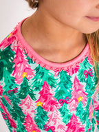 Close-up of a child wearing a bright pink and green Christmas tree pattern top with a ruffled neckline.