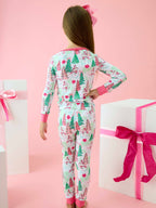A child wearing a long-sleeve pajama set with a Christmas tree and snowman print, shown from the back against a pink background with gift boxes.