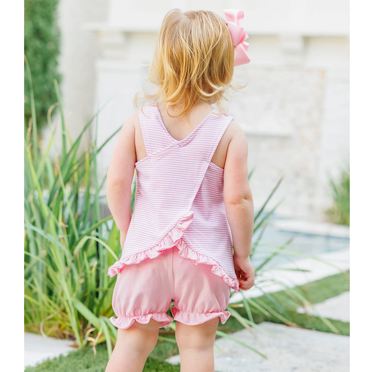 Little girl showing the back of a light pink striped sleeveless bloomer set with ruffles.