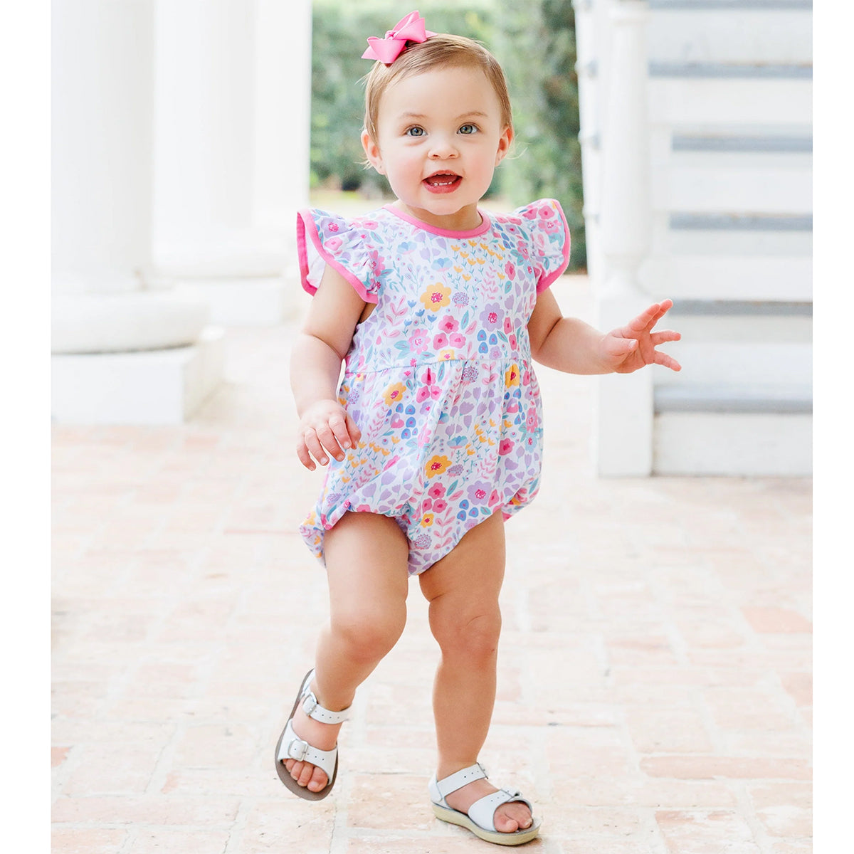 Baby girl in a summer floral bubble, pink hairbow and white sandals.