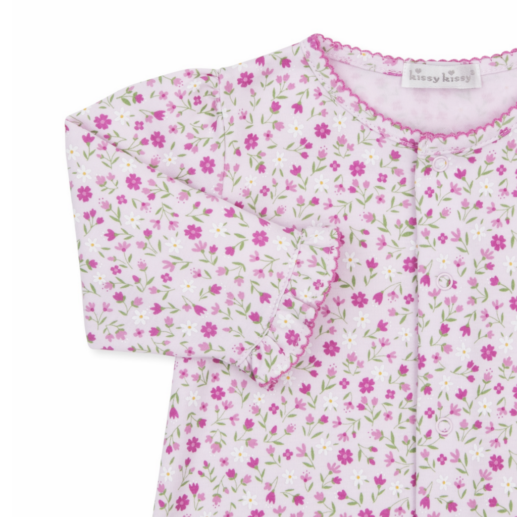A baby girl pink converter gown closeup with a Kissy Kissy brand label, floral print, hot pink trim, and ruffles at the wrists.