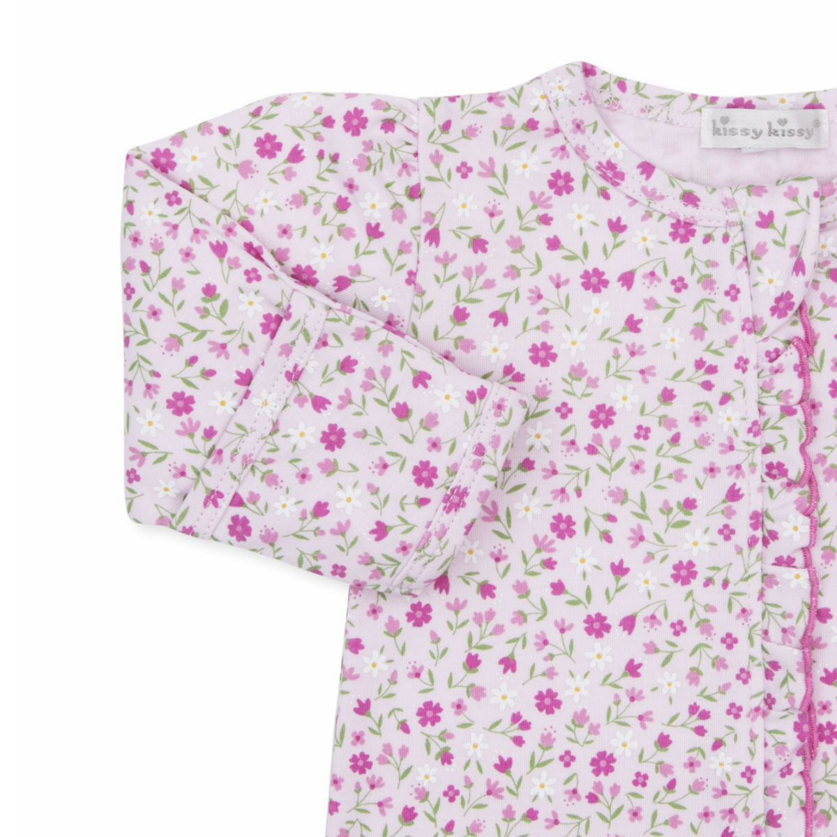 A baby girl pink footed sleeper closeup with a Kissy Kissy brand label, floral print, a ruffle down the zipper front, hot pink trim, and mitten cuffs.