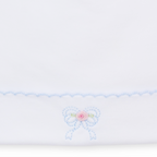 A white knit newborn baby girl hat closeup featuring a light blue scalloped trim and a small embroidered bow with a pink rose center.