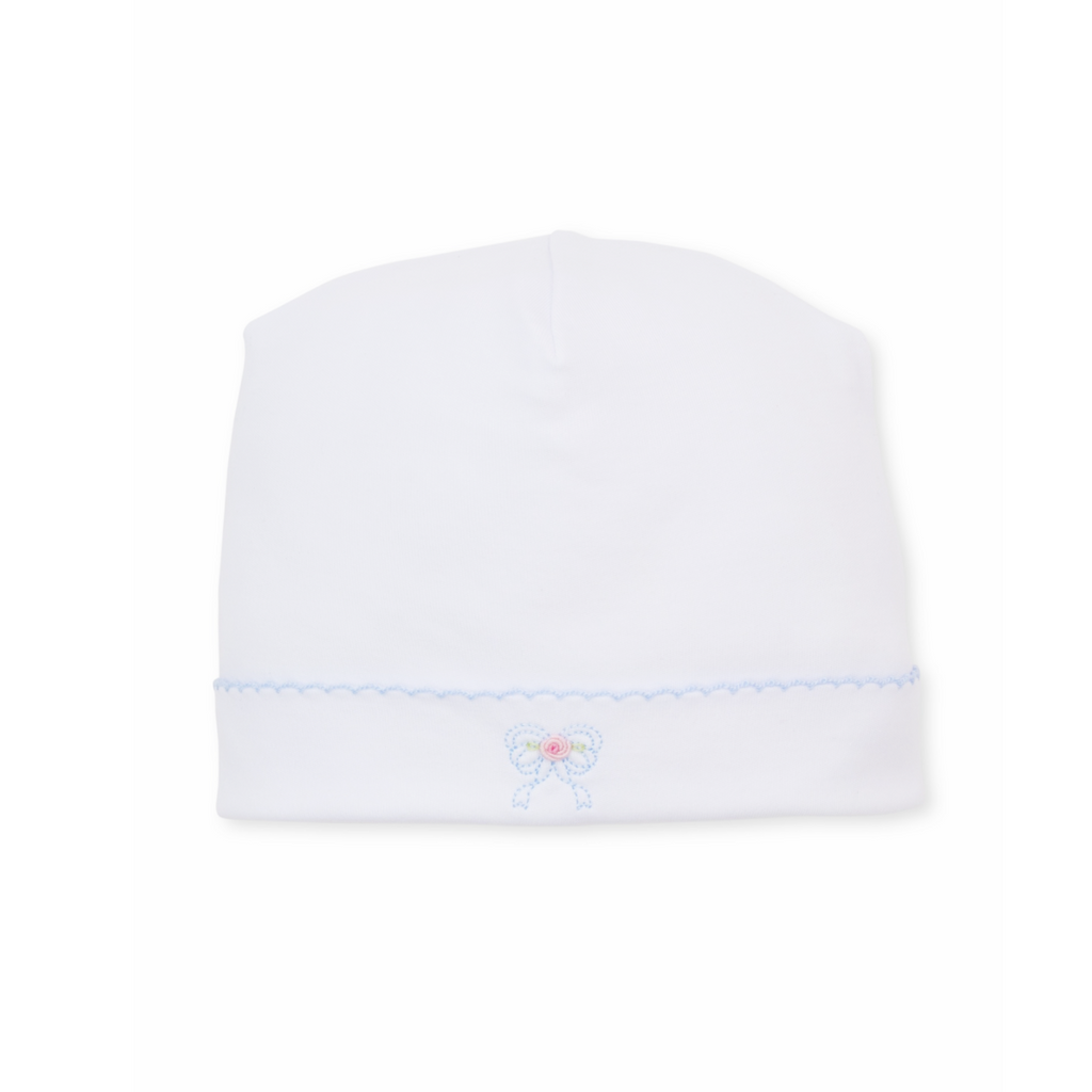 A white knit newborn baby girl hat featuring a light blue scalloped trim and a small embroidered bow with a pink rose center.