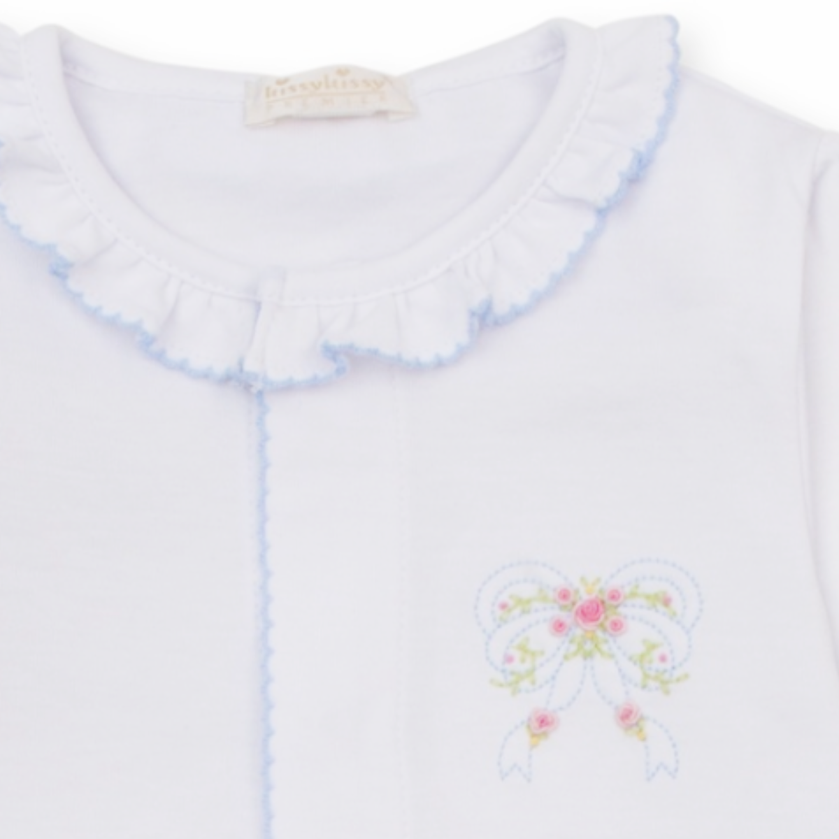 A white long-sleeve baby girl converter gown closeup with ruffled collar and cuffs, light blue trim and a delicate embroidered bow with pink rosettes. 