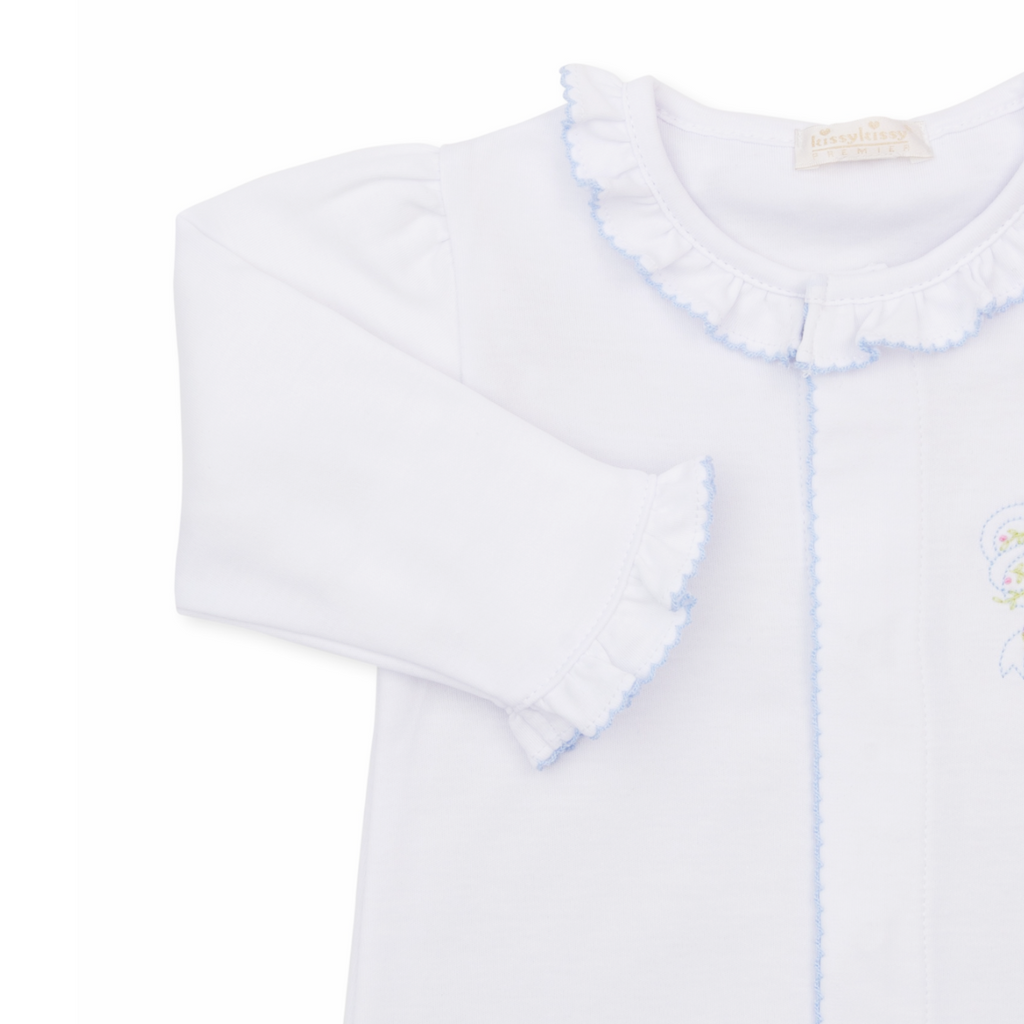 A white long-sleeve baby girl sleep sack with ruffled collar and cuffs, light blue trim and a delicate embroidered bow with pink rosettes. 