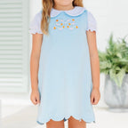 A little girl wearing a light blue bubble with a pumpkin bow applique on the chest and a long sleeve white knit shirt with Peter Pan collar.