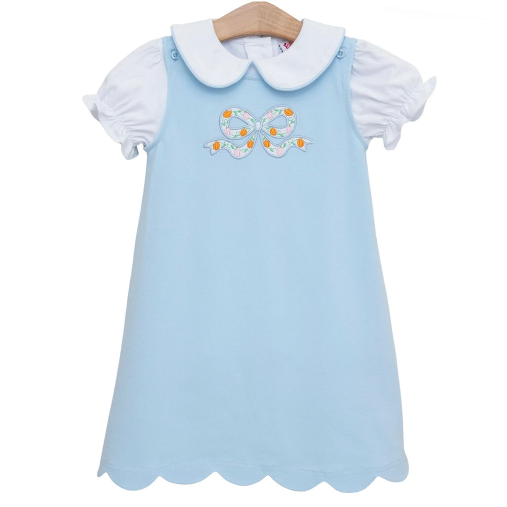 A light blue toddler girl dress outfit with a white Peter Pan collar short-sleeve knit shirt and a blue A-line jumper featuring an applique bow with embroidered pumpkins.