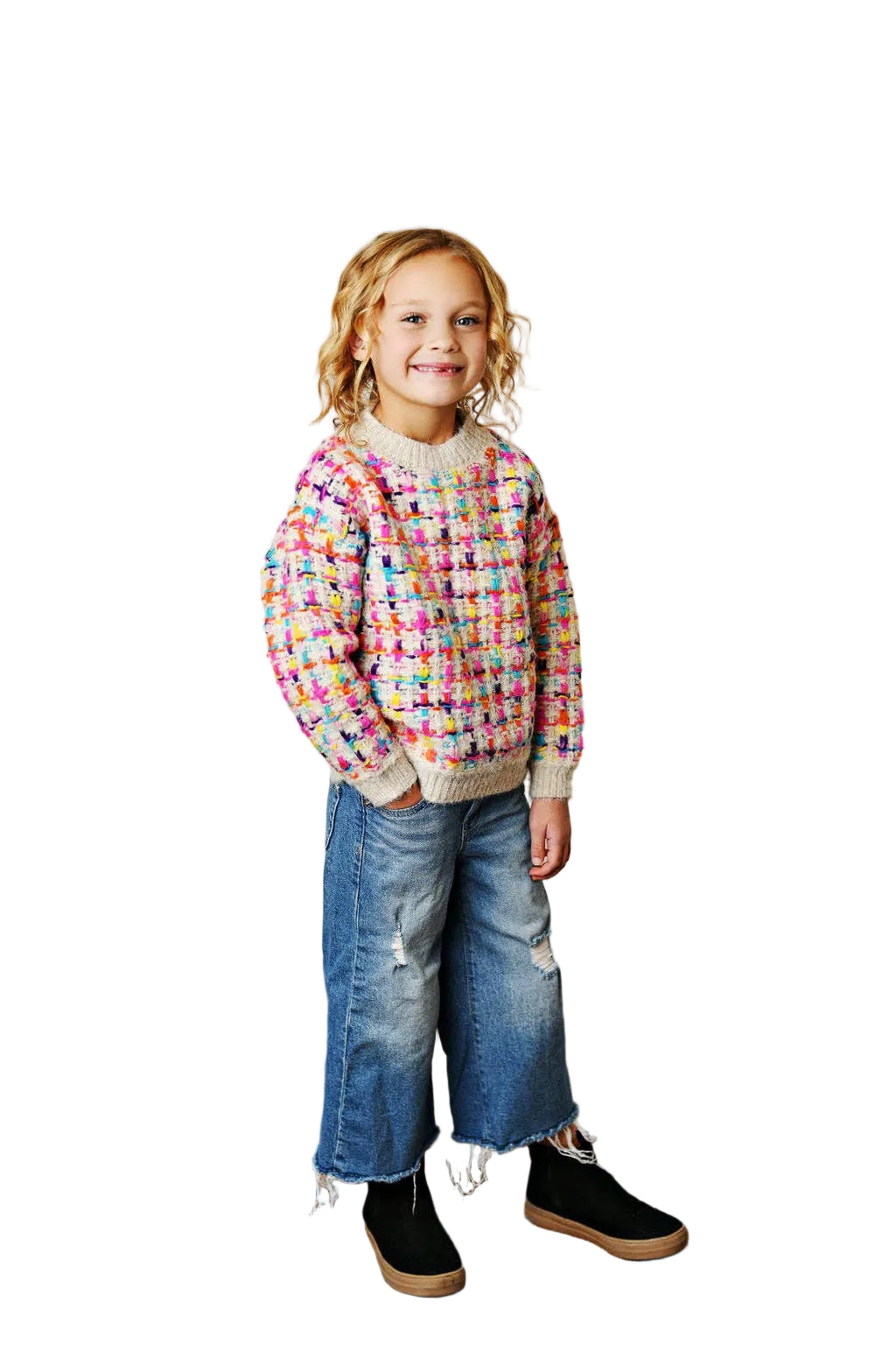 Child wearing a colorful sweater and blue jeans standing on a wooden floor.