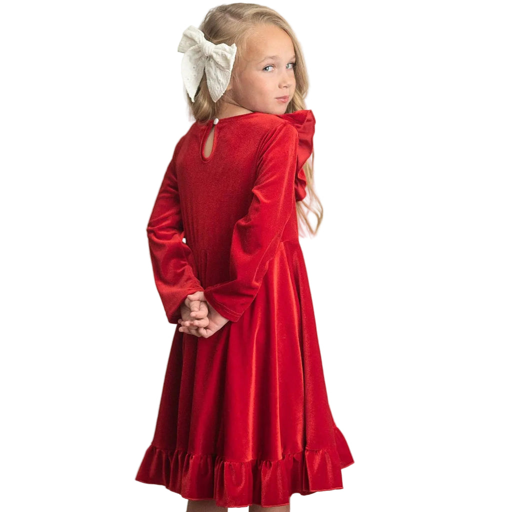 Young girl wearing a red dress with long sleeves against a white wooden panel background