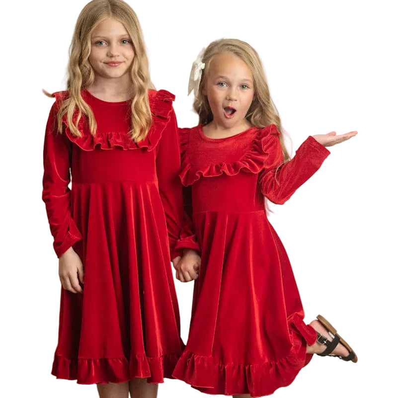 Two young girls wearing red dresses standing against a white wall.