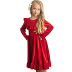 Young girl wearing a red dress with ruffled details against a white wooden paneled wall.