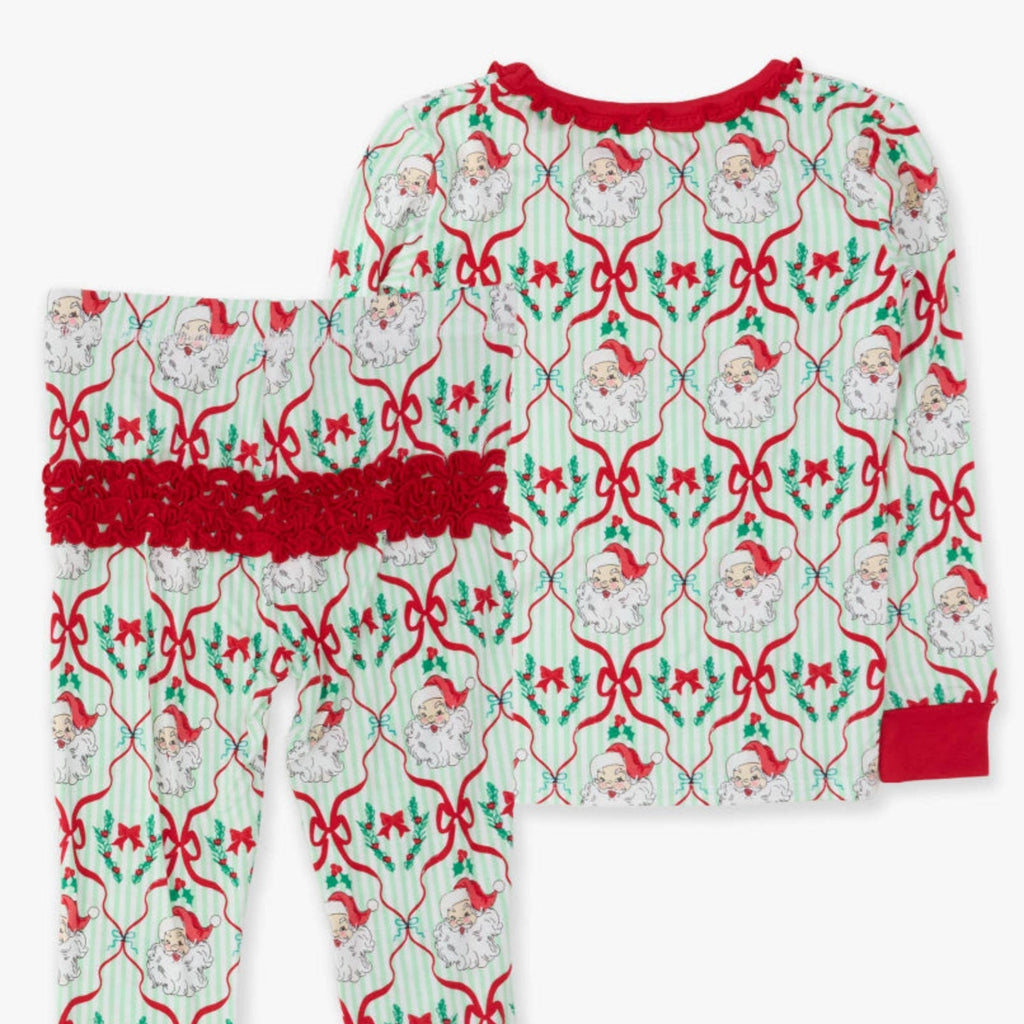 A two-piece children's pajama set featuring a long-sleeve top and matching pants with a festive Christmas print of Santa Claus, red bows, holly, and green leaves on a white background with red trim.