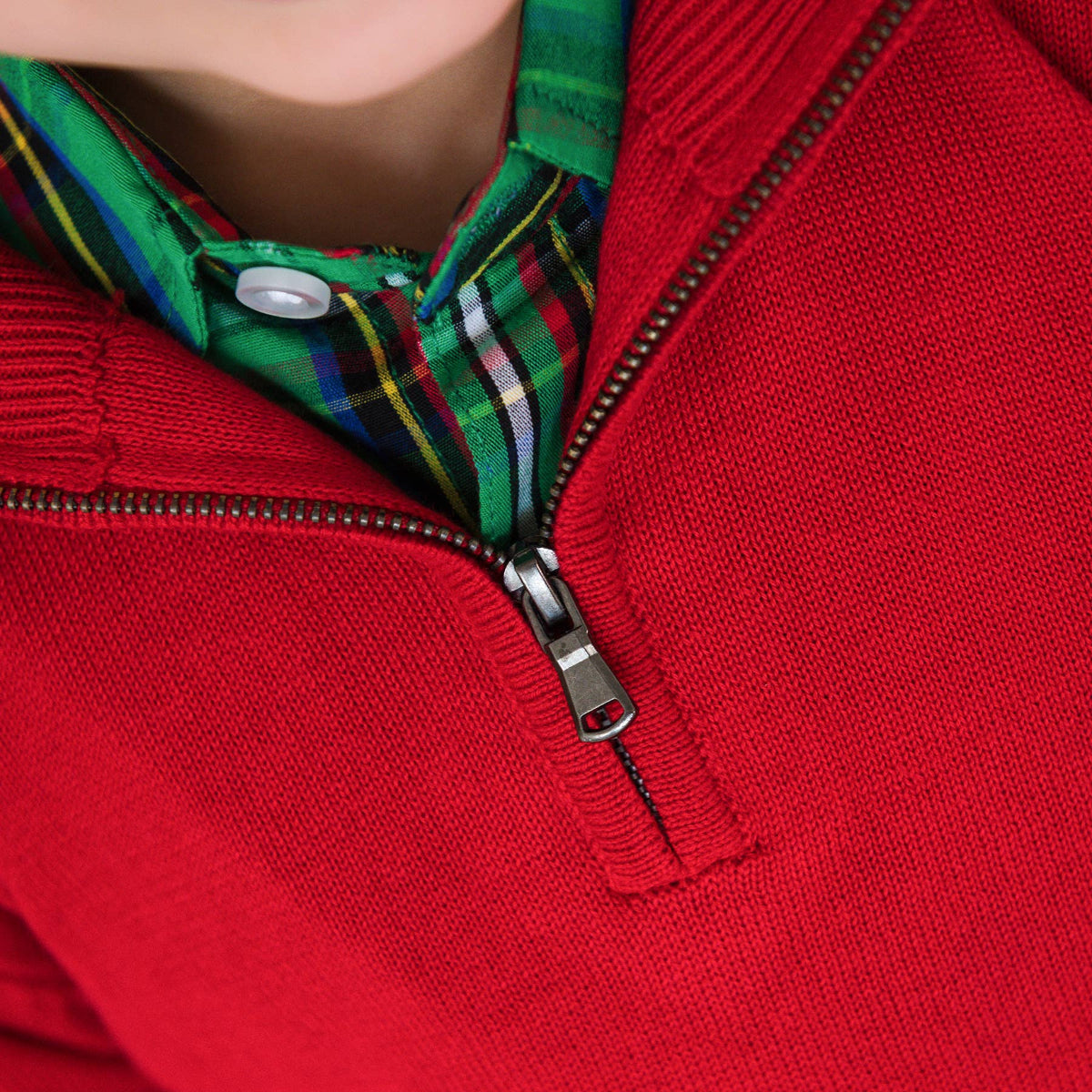 Close-up of a red sweater with a zipper and plaid collar.