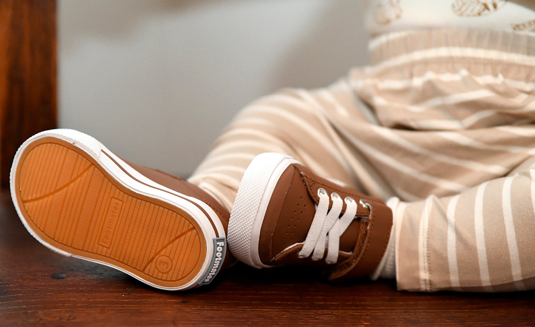 A close-up lifestyle shot of a child's legs wearing brown leather Footmates sneakers with white laces