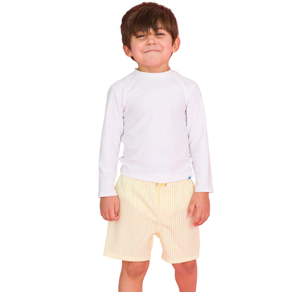 Child wearing a white long-sleeve rashguard top and yellow striped swim trunks.