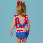 Little girl wearing a red, white and blue patriotic 2-piece swimsuit with ruffles.
