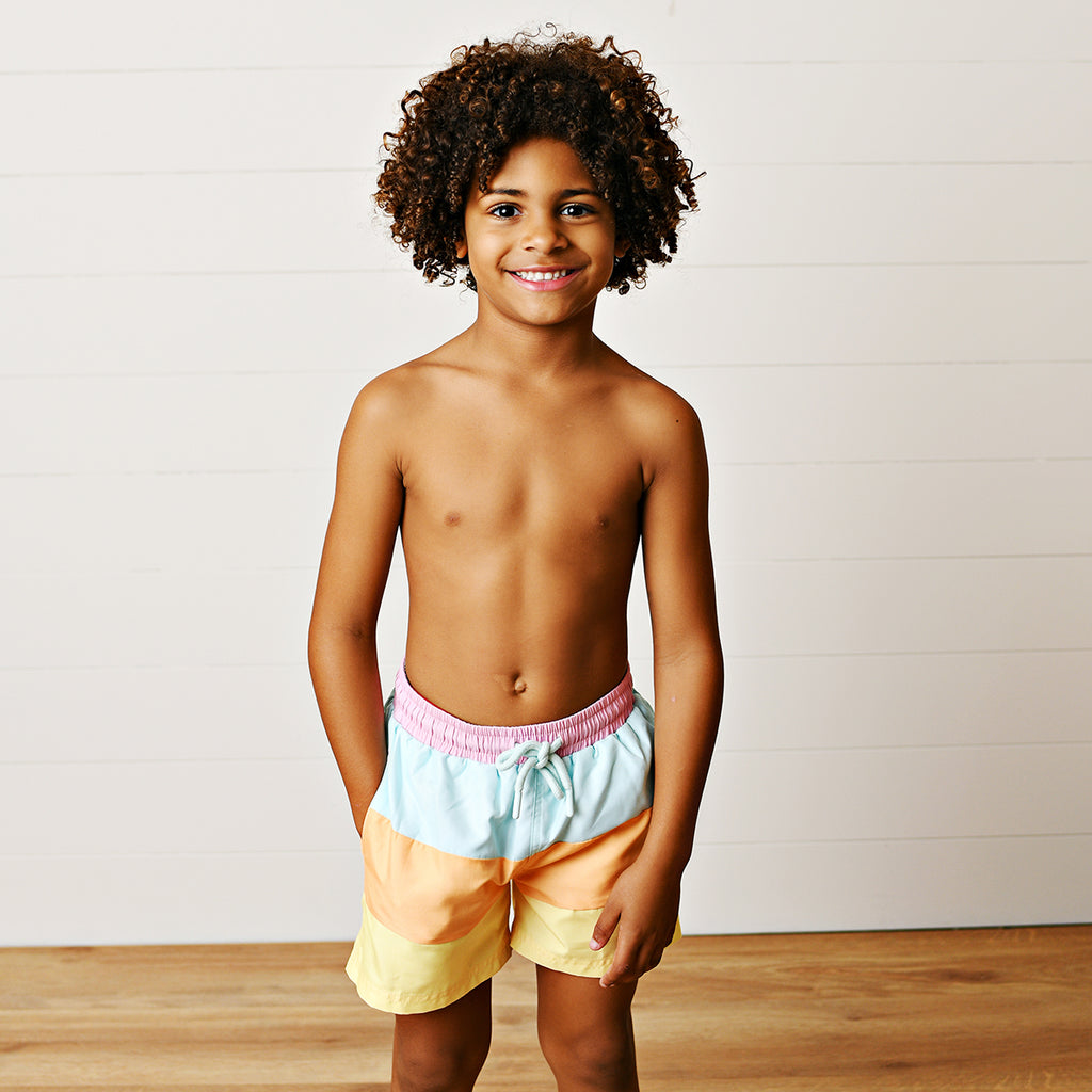 Boy wearing color-blocked swimsuit in yellow, orange, aqua and pink with a drawstring